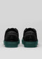 Un paio di SO0002 The Wanderer low top sneakers con suola in gomma verde scuro, visualizzate dalla vista posteriore su uno sfondo grigio chiaro.