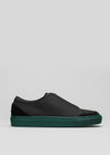 Black leather slip-on sneaker with a green sole on a white background.