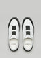 Un paio di sandali slip-on bianchi e neri in pelle, con l'etichetta "SO0005 Challenger23" visibile sulla soletta, su sfondo grigio chiaro.