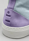 Nahaufnahme eines TH0008 KT's Kicks High-Top-Canvas-Schuhs, der an der Ferse einen lilafarbenen Wildlederaufnäher mit Logoprägung vor grauem Hintergrund zeigt.