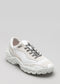 Una singola sneaker bassa V6 Leather Color Mix White con accenti grigi e suola spessa su sfondo grigio.