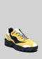 Gelber und schwarzer Low-Top-Sneaker L0003 mit weißen Schnürsenkeln und einer klobigen Sohle auf grauem Hintergrund.
