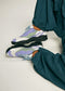 Person trägt V13 Leather Color Mix Fuchsia low top sneakers, gepaart mit teal baggy pants, stehend auf einem neutralen Hintergrund.