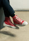 A person wearing red TH0008 KT's Kicks custom high-top sneakers sitting with one foot flat on the ground and the other foot resting on its heel.