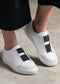 A pair of V10 White Leather w/Blue sneakers with black elastic bands on a person wearing cropped black pants.