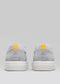 Rückansicht des grauen V2 Low Top sneakers mit weißer Sohle und einem gelben quadratischen Aufnäher an der Ferse.