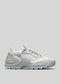 A white low-top sneaker with a chunky, sculpted sole and lace-up front, showcased against a V8 Leather Color Mix Grey background.