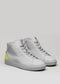 Un par de MH0005 Be Your Own Star de caña alta sneakers en piel blanca con un acento amarillo neón en el talón, sobre un fondo gris claro.