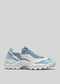 The L0024 by Bárbara is a white and blue sneaker with a chunky sole, crafted from premium Italian leathers. It features a lace-up closure against a plain gray background.