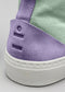 Close-up of a V10 Lilac & Sage Green sneaker with a white sole and purple suede heel tab embossed with a logo, adjacent to a green fabric upper.