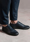 Close-up of a person's feet wearing SO0016 Black W/ Orange low top sneakers and navy pants on a textured floor.