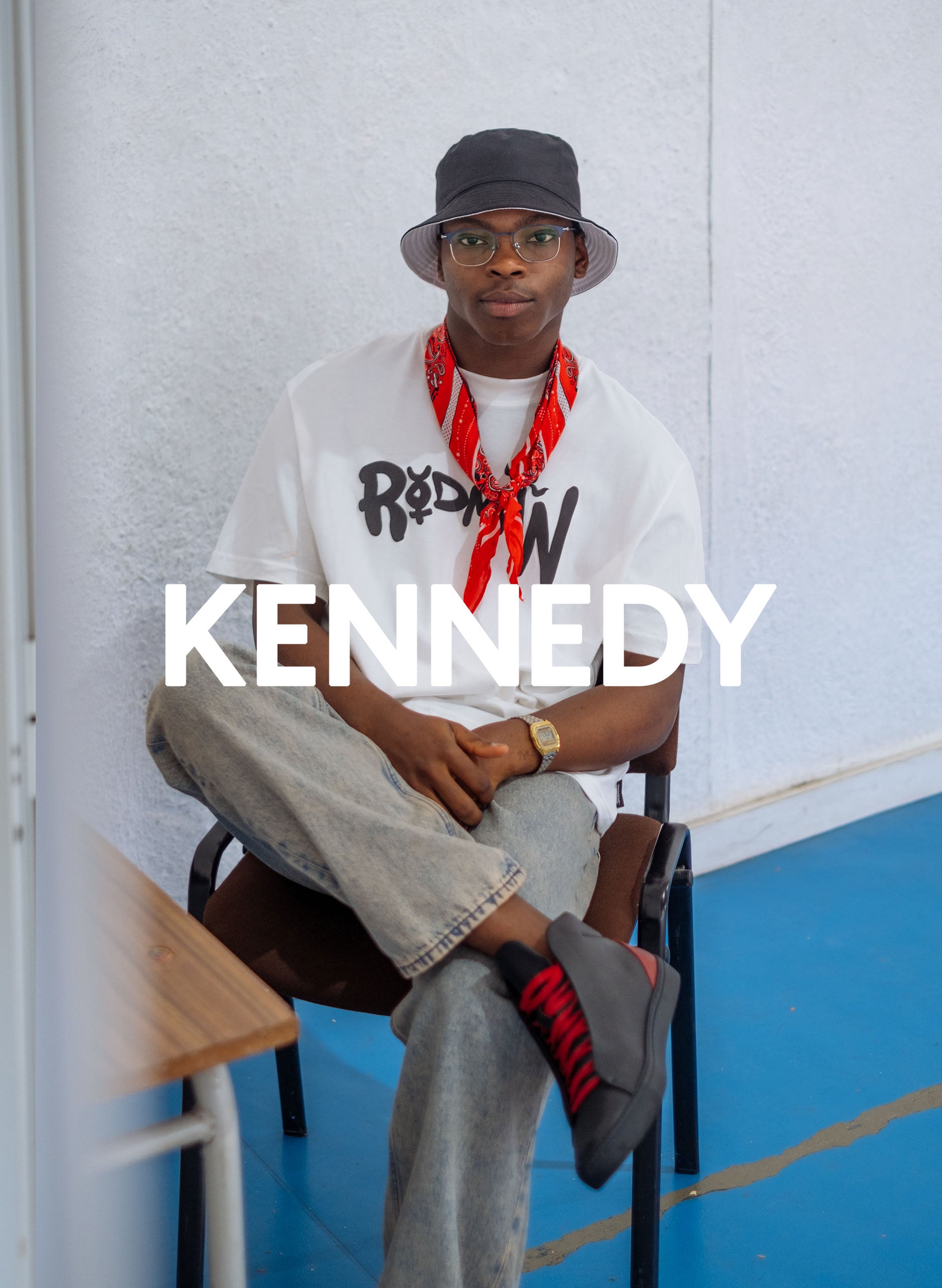 Kennedy sitzt auf einem Stuhl und trägt Diverge sneakers, die im Rahmen des Imagine-Projekts soziale Auswirkungen und maßgeschneiderte Schuhe präsentiert.