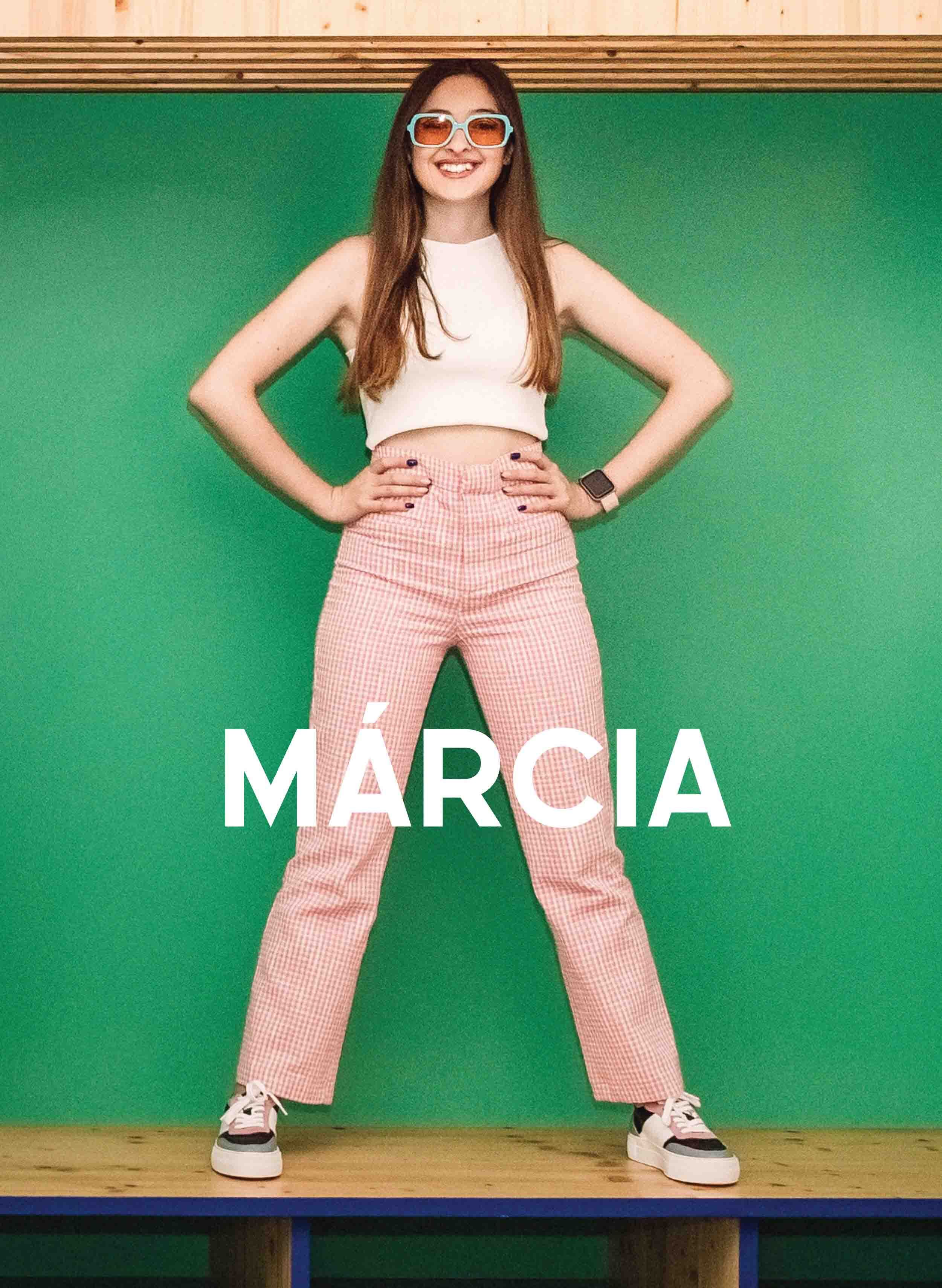 Márcia in a white top and red checked trousers, smiling with her hand on her waist, wearing Diverge sneakers, promoting social impact and custom shoes throught the imagine project.