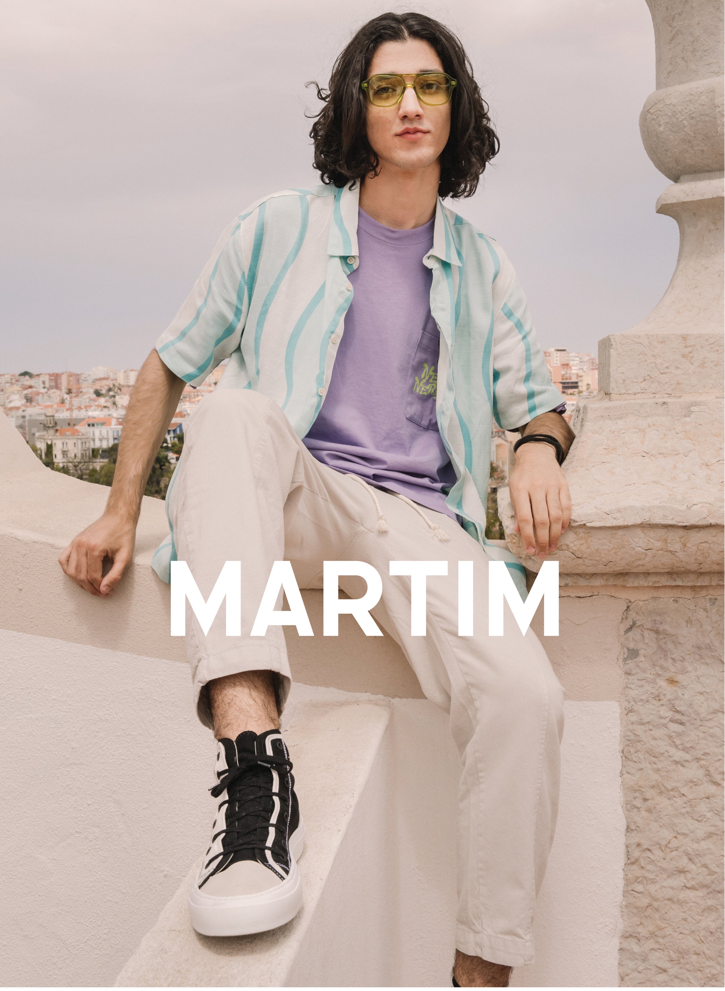 Martim sentado en una pared con un paisaje, vistiendo Diverge sneakers, promoviendo el impacto social y el calzado personalizado.  