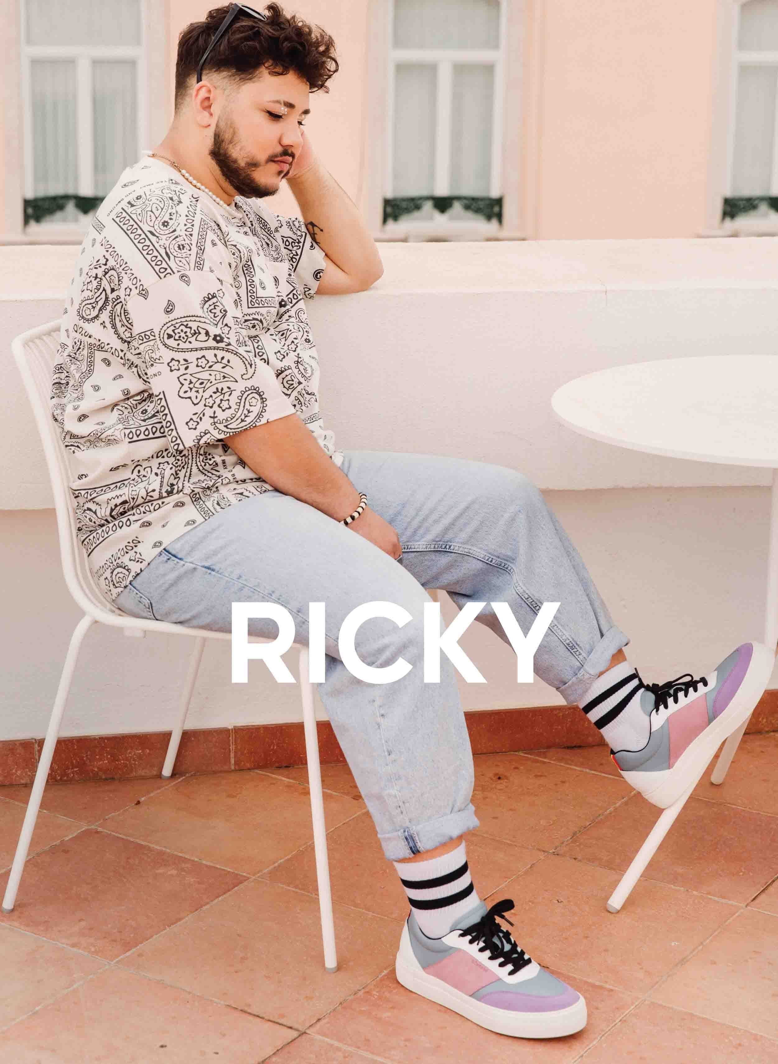 Ricky sentado en una silla mirando su costumbre Diverge sneakers, promoviendo el impacto social y el calzado personalizado a través del proyecto Imagine.   