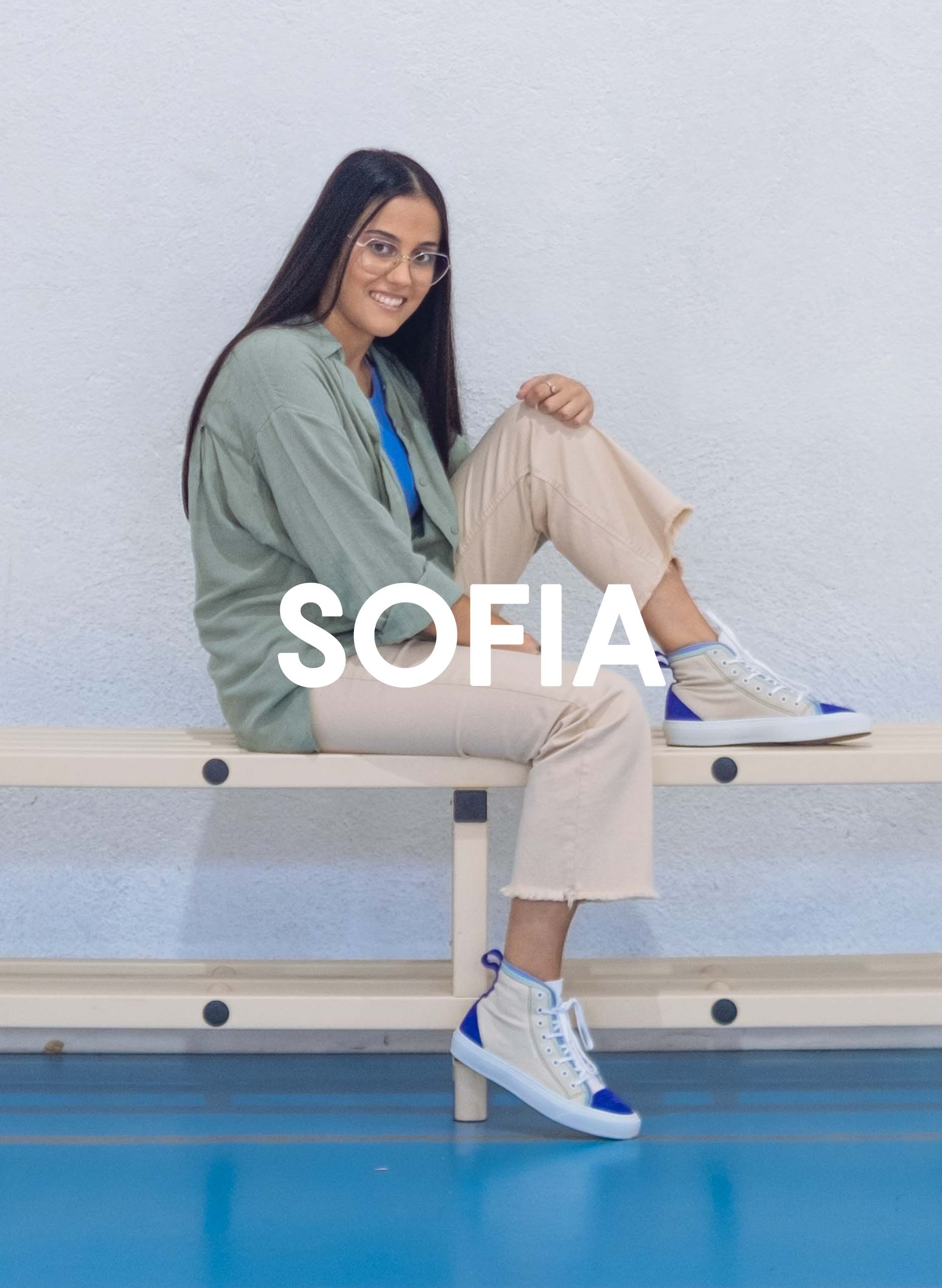 Sofia, vêtue d’une chemise verte et d’un pantalon beige, assise sur un banc avec Diverge sneakers, promouvant l’impact social et les chaussures personnalisées à travers le projet Imagine.