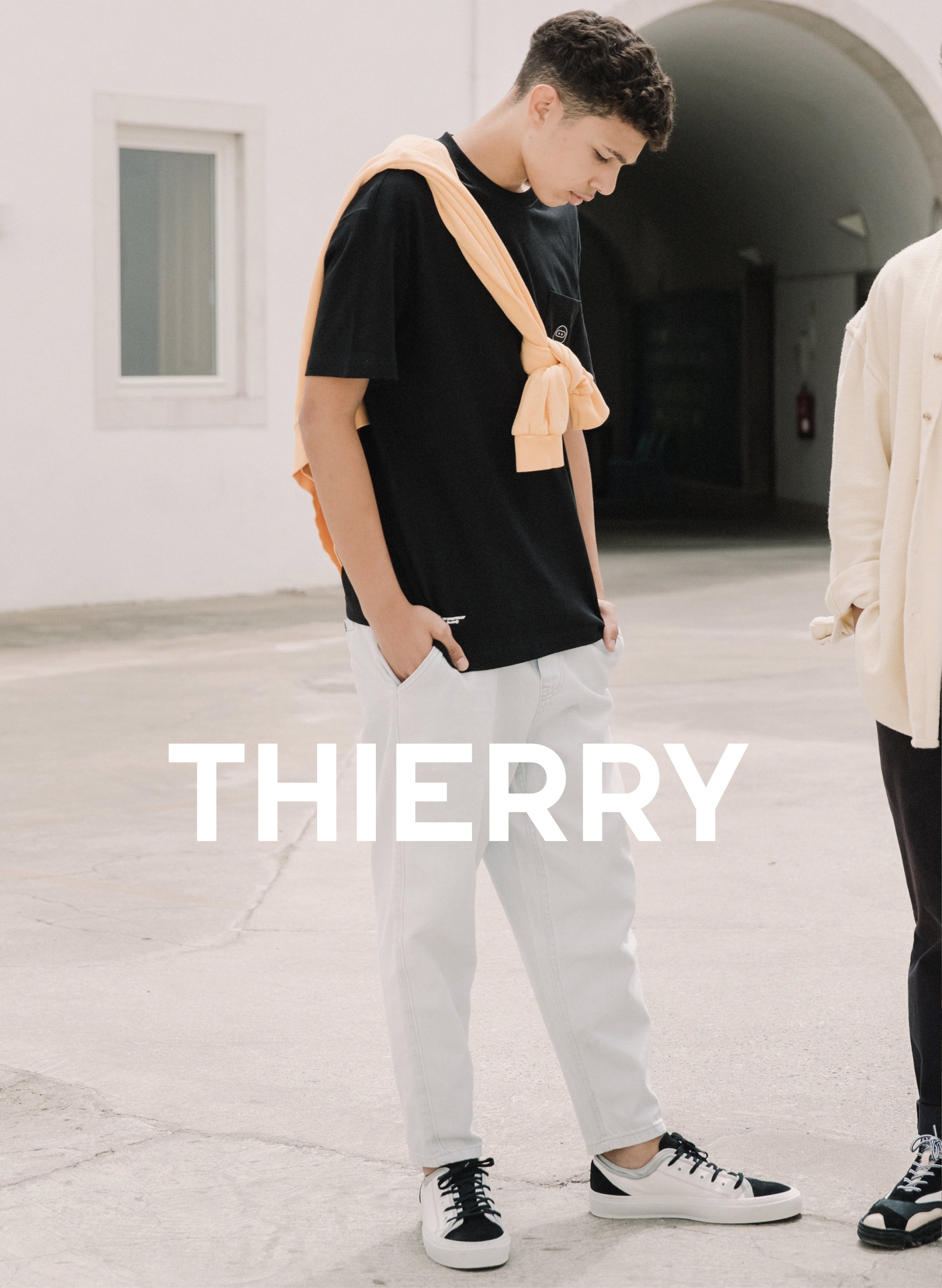 A man looking down in a black sweater and white pants with custom shoes named Thierry, showcasing Diverge sneakers and promoting social impact.