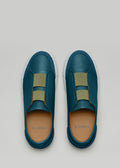 Un par de V15 Ocean Blue Leather W/ Grey slip-on sneakers con detalles en verde oliva, sobre un fondo gris claro.