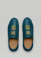 Un par de V15 Ocean Blue Leather W/ Grey slip-on sneakers con detalles en verde oliva, sobre un fondo gris claro.