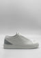 The ML0130 White W/ Grey are sleek, minimalist white sneakers handcrafted in Portugal from premium Italian leathers. They feature a smooth design with a light gray heel accent and white laces, displayed on a plain white background.