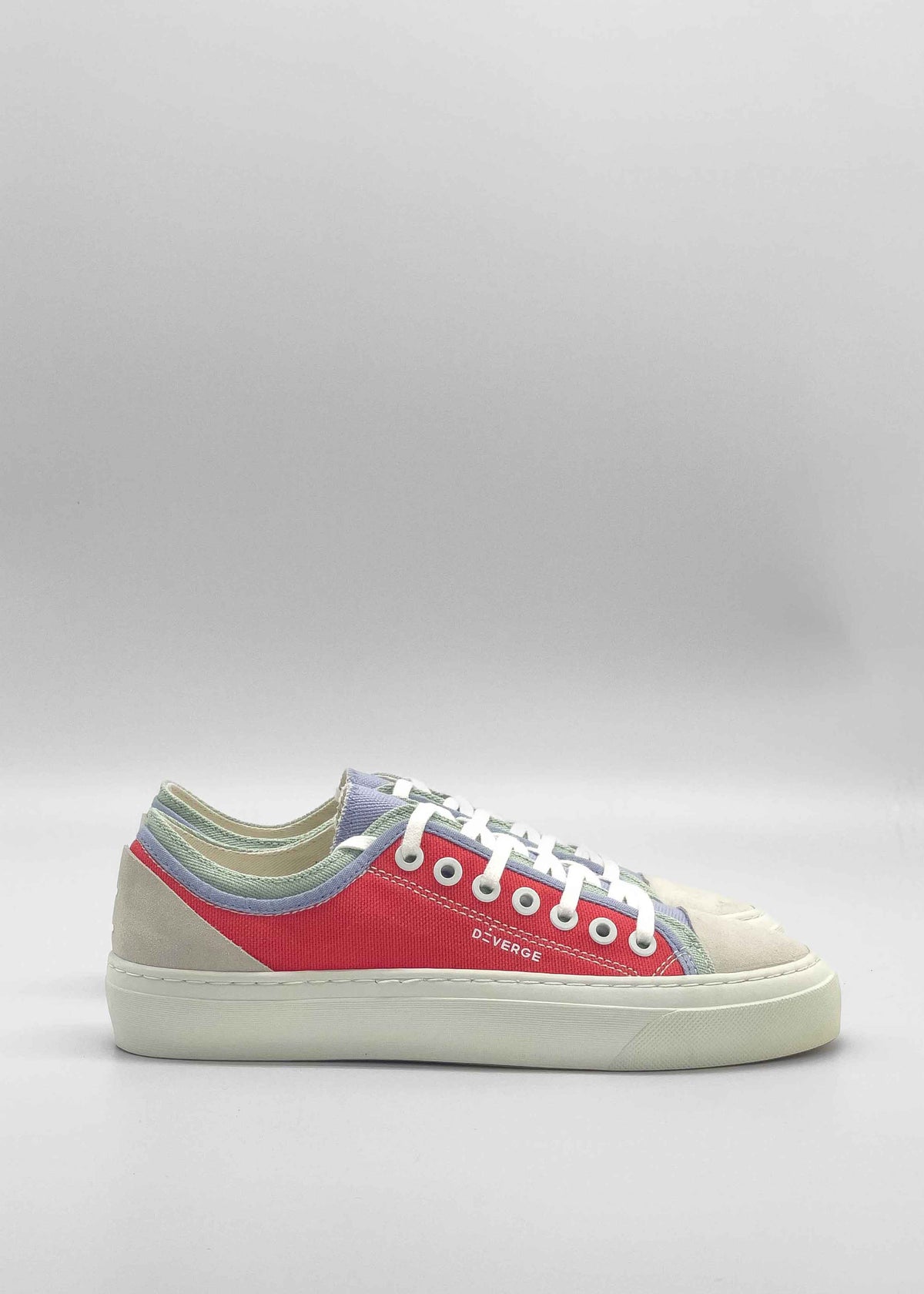 A side view of the TL0008 Geranium & Lilac sneaker shows its casually chic design with a white sole, red and light blue fabric, white laces, and metal eyelets. Ethically made to order from premium Italian leathers and expertly handcrafted in Portugal, it's set against a plain gray background.