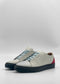 The ML0139 White W/ Red sneakers showcase white low-tops with light blue laces, black soles, and red heel accents, crafted from premium Italian leathers and handcrafted in Portugal, elegantly set against a simple gray background.