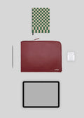 Flaches Layout eines Tablets, M Leather Pouch Bordeaux, Airpods, Stifts und Notizbuchs mit einem grün karierten Cover auf einem hellgrauen Hintergrund, mit stilvollen Lederwaren.