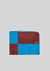 M Patchwork Pouch Bordeaux & Blue Brieftasche mit blauen und roten Ledereinsätzen und einem Reißverschluss, mit einem kleinen Logo auf der Vorderseite.