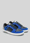 A pair of M0003 by Luís low top sneakers in blue and black suede with white soles and blue laces on a gray background.