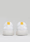 Rückansicht des V3 White & Bone Low Top sneakers mit gelben quadratischen Laschen an den Fersen vor einem neutralgrauen Hintergrund.