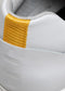 Close-up of the heel of a V3 White & Bone low top sneaker featuring embossed text and a yellow textured patch.