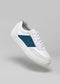 Zapatilla V9 blanca y azul petróleo con lengüeta roja en el talón sobre fondo gris, perfecta como calzado personalizado.