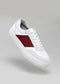 A single white low top sneaker with a red accent on the side, displayed against a neutral gray background, N0004 Talent.