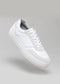A Now White Canvas low-top vegan sneaker with a thick sole, photographed on a neutral gray background.