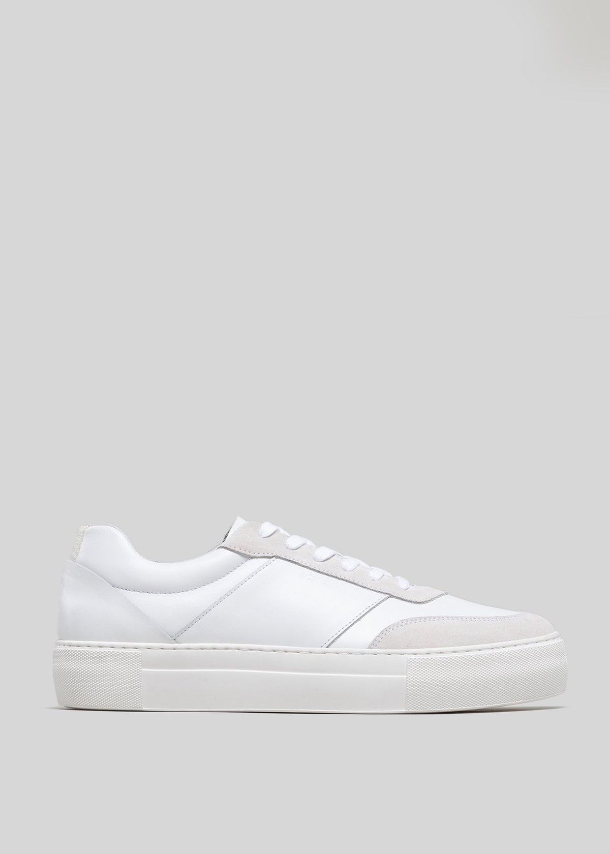 Vista laterale di una sneaker bassa Now White Canvas con suola spessa, visualizzata su uno sfondo grigio chiaro.