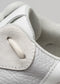 Primer plano de una zapatilla baja de lona blanca en el que se aprecian las costuras, el tejido texturizado y los cordones.
