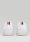 Vista trasera de sneakers de cuero blanco con una pequeña franja arco iris en el talón sobre un fondo gris claro.
