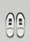 Un paio di V6 White Leather w/Black slip-on sneakers con elastici neri, visti dall'alto su uno sfondo grigio.