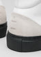 Nahaufnahme eines V1 White Leather w/Bone Schuhabsatzes mit "chic"-Prägung auf beigem Wildleder vor einem grauen Hintergrund.