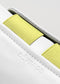 Close-up of a white low-top sneaker with yellow accents and the brand name "SO0001 JL Fluo-Corra" embossed on it.