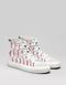 Une paire de chaussures blanches en toile avec un motif abstrait rouge, sur fond gris.